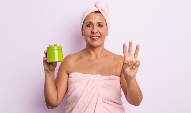 Ładna kobieta w średnim wieku, uśmiechnięta i wyglądająca przyjaźnie, pokazując numer trzy. koncepcja prysznica i produktu do włosów
