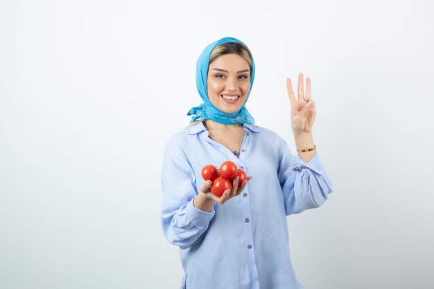 Ładna kobieta w szal pokazujący numer trzy z ręką i trzymając czerwone pomidory