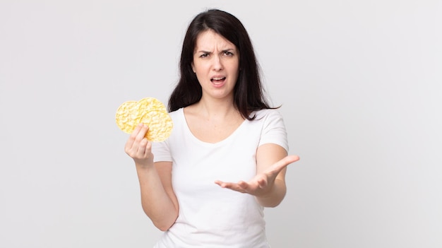 Zdjęcie Ładna kobieta wyglądająca na złą, zirytowaną i sfrustrowaną, trzymająca dietetyczne ciastka ryżowe