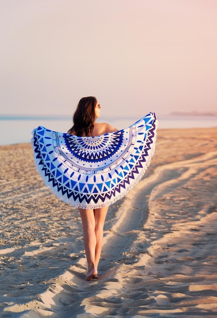 Ładna kobieta z mandalą okrągłym gobelinem plażowym na wybrzeżu oceanu
