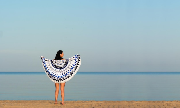 Ładna kobieta z mandalą okrągłym gobelinem plażowym na wybrzeżu oceanu