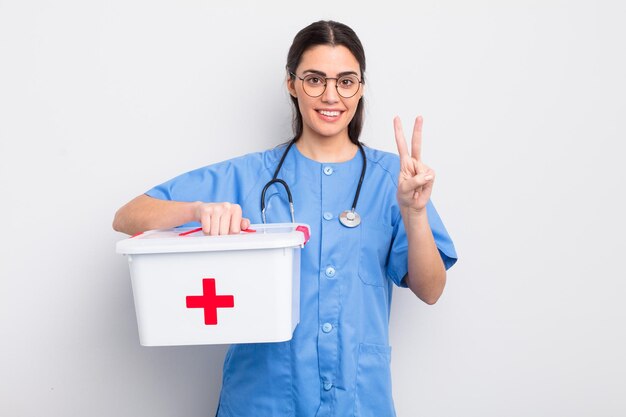 Ładna latynoska kobieta, uśmiechnięta i wyglądająca przyjaźnie, pokazująca pielęgniarkę numer dwa i zestaw pierwszej pomocy