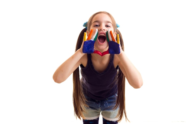 Ładna mała dziewczynka w czarnej koszuli i dżinsach z dwoma kucykami i kolorowymi rękami krzyczącą w studio