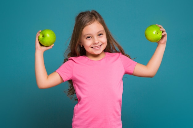 Ładna, mała dziewczynka w koszulce z brązowymi włosami trzyma owoce