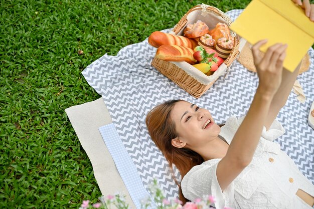 Ładna młoda Azjatka piknikuje w ogrodzie, relaksując się i relaksując na kocu piknikowym