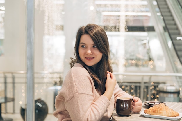 Ładna młoda dziewczyna siedzi z filiżanką kawy w kawiarni Piękne kobiety cieszą się kawą w kawiarni