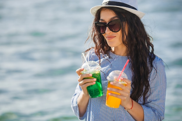 Ładna młoda kobieta pije koktajl na plaży. Atrakcyjna dziewczyna oferuje drinka. Piękna kobieta pije lemoniadę