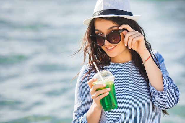 Ładna młoda kobieta pije koktajl na plaży. Atrakcyjna dziewczyna oferuje drinka. Piękna kobieta pije lemoniadę