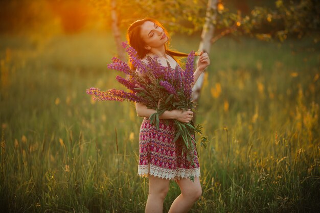 Ładna młoda kobieta w polu przy zmierzchem. trzymając kwiaty