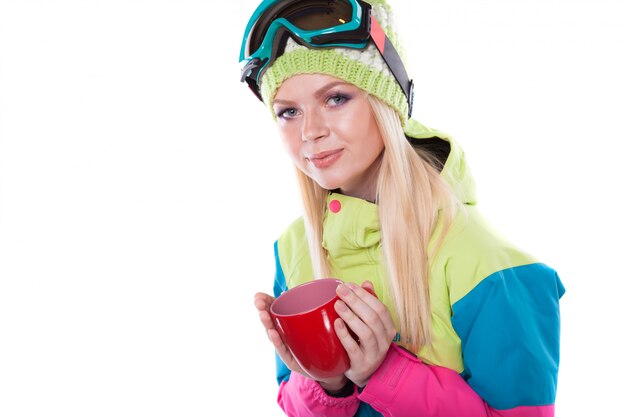 Ładna młoda kobieta w stroju narciarskim i narciarskich szkłach trzyma czerwonego puchar