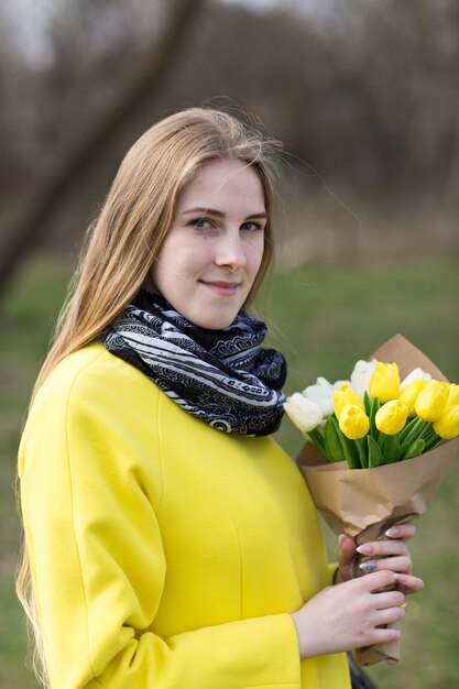 Ładna młoda kobieta w żółtym płaszczu z białymi i żółtymi kwiatami