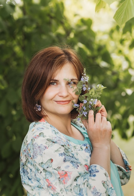 Ładna młoda kobieta z małym bukietem polnych kwiatów w lecie na łonie natury. Portret z bliska