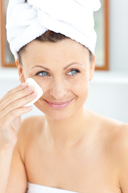 Zdjęcie Ładna młoda kobieta z ręcznikową kładzeniem kremowa na jej twarzy w łazience