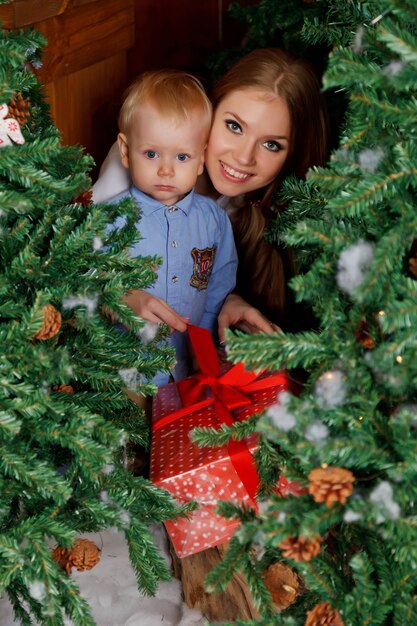 Ładna Młoda Kobieta Z Rocznym Dzieckiem Bawiącym Się Drzewem Szczęśliwego Nowego Roku. Mama Z Uroczym Synem W Pokoju Urządzonym Wesołych świąt. Są Uśmiechnięci I Szczęśliwi. Koncepcja Rodzinnego Wypoczynku. Skopiuj Miejsce