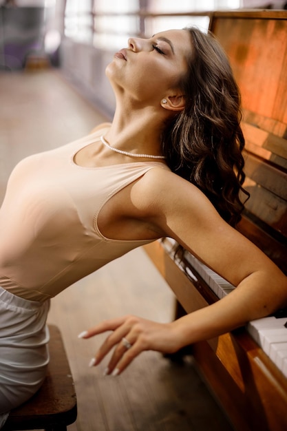 Ładna młoda tancerka siedzi przy pianinie w studiu tanecznym