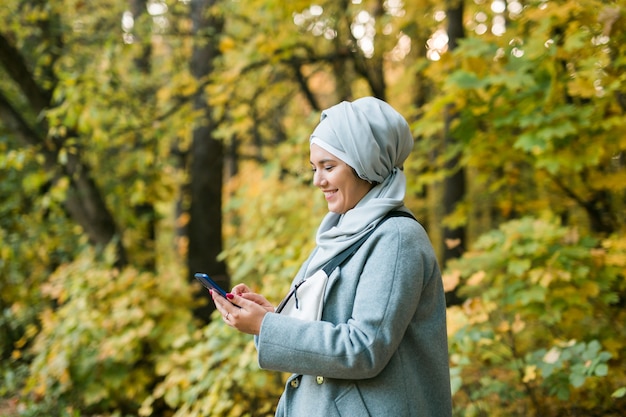 Ładna muzułmańska kobieta korzystająca z telefonu komórkowego na zewnątrz arabska kobieta ubrana w hidżab za pomocą smartfona islamski