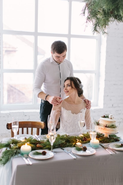 Ładna panna młoda i pan młody w pobliżu weselnego stołu z tortem ślubnym, niebieskie świece i dekoracje sosnowe