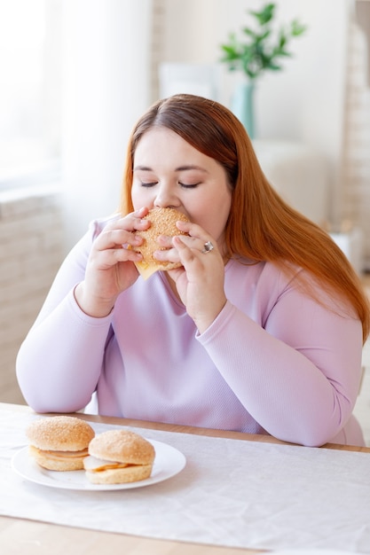 Ładna pulchna kobieta je smacznego burgera będąc głodna