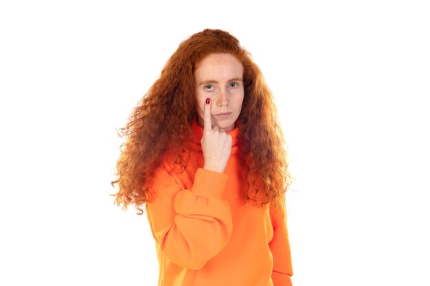 Zdjęcie Ładna ruda kobieta ubrana w pomarańczową koszulkę stojącą na białym tle wskazująca na oko obserwujące twój gest