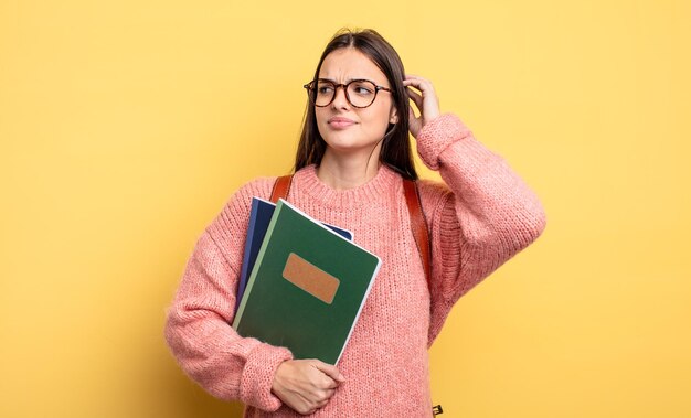 Ładna studentka czuje się zdziwiona i zdezorientowana, drapiąc się po głowie