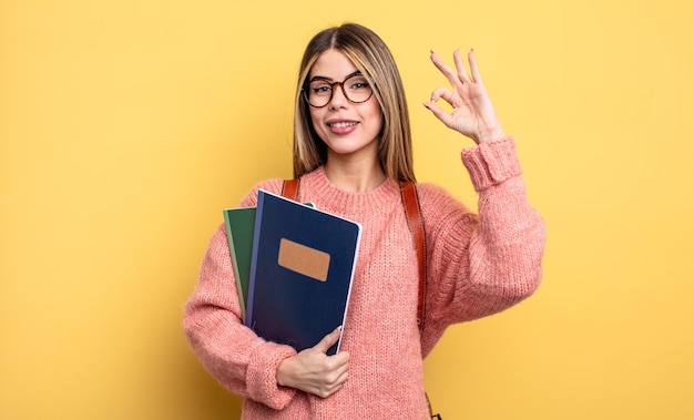 Ładna studentka kobieta czuje się szczęśliwa, pokazując aprobatę w porządku gestem. książki i plecak