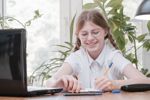 Ładna uczennica studiująca pracę domową podczas lekcji online w domu, dystans społeczny podczas kwarantanny, samoizolacja, koncepcja edukacji online, uczeń domowy. Edukacja online na odległość