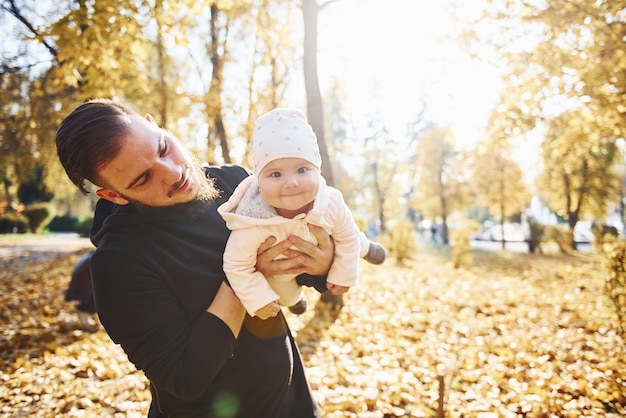 Ładne światło słoneczne. Ojciec w ubraniu ze swoim dzieckiem jest w pięknym jesiennym parku.