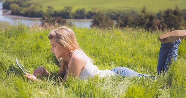 Ładny blondynki lying on the beach na trawie używać jej pastylkę na słonecznym dniu w wsi