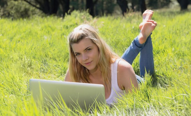 Zdjęcie Ładny blondynki lying on the beach na trawie używać laptop ono uśmiecha się przy kamerą