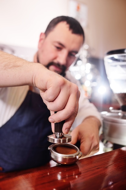 Ładny brodaty barista mężczyzna trzyma uchwyt z kawą mieloną