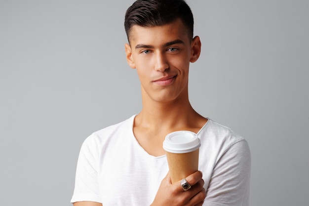 Ładny brunetka młody człowiek trzyma filiżankę kawy nad szarym