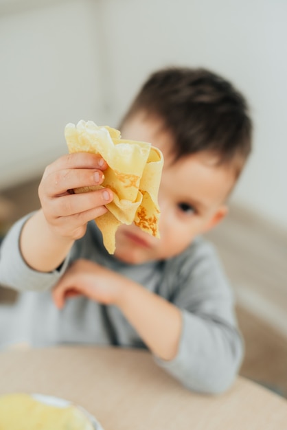 Ładny chłopak jedzenie pyszne naleśniki siedzi przy stole na jasnym tle ładny