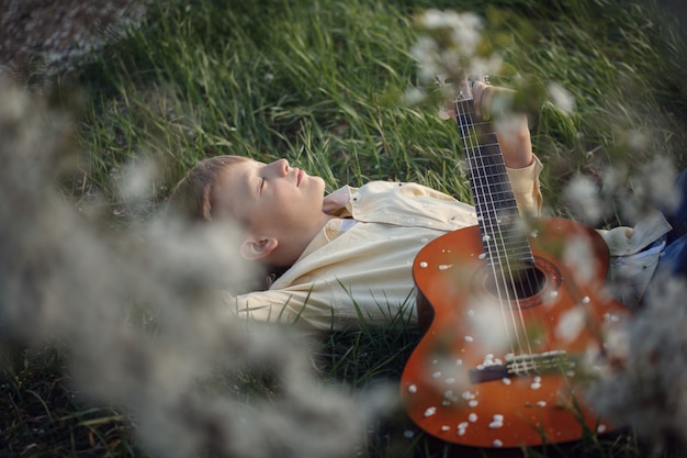 Zdjęcie Ładny chłopak leży na trawie z gitarą na zachód słońca