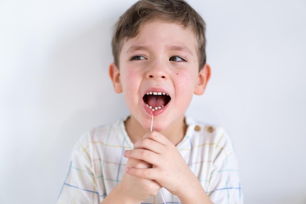 Ładny chłopak wyciągając luźny ząb za pomocą nici dentystycznej. Pierwszy ząb mleczny chłopca jest luźny. Ból zęba. Proces usuwania zęba dziecka. Emocje dziecka