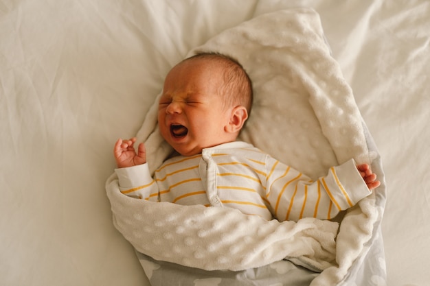 Ładny emocjonalny noworodka mały chłopiec płacze w łóżeczku. Brzuch boli i emocje