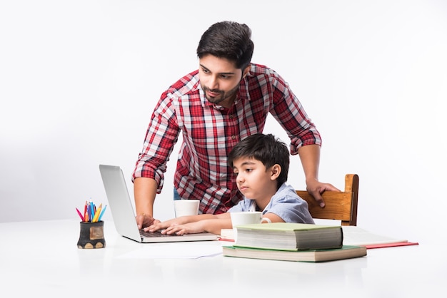 Ładny indyjski chłopiec z ojcem lub korepetytorem odrabiania lekcji w domu za pomocą laptopa i książek - koncepcja edukacji online