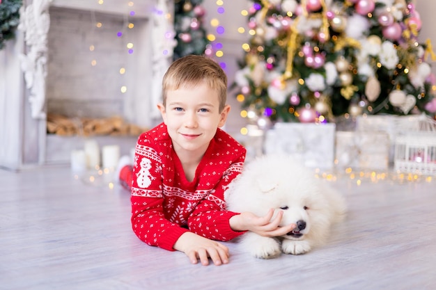 Ładny mały chłopczyk z białym szczeniakiem Samoyed w pobliżu choinki, koncepcja wakacje, nowy rok