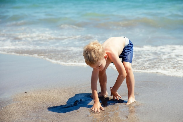 Ładny mały chłopiec blondynka bawi się na plaży nad morzem jest szczęśliwy Koncepcja letnie wakacje odpoczynku