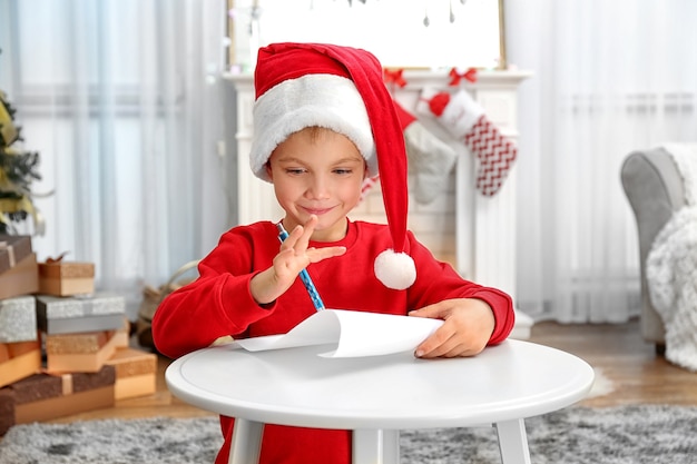 Ładny mały chłopiec pisze list do Świętego Mikołaja przy stole