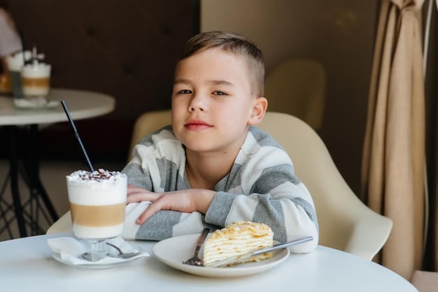 Ładny mały chłopiec siedzi w kawiarni i patrząc na zbliżenie ciasta i kakao. Dieta i prawidłowe odżywianie.