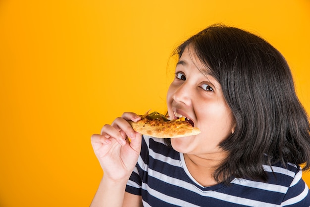 Ładny mały indyjski lub azjatycki dziecko dziewczynka jedzenie smaczne Burger, kanapkę lub pizzę w talerzu lub polu. Stojący na białym tle na niebieskim lub żółtym tle.