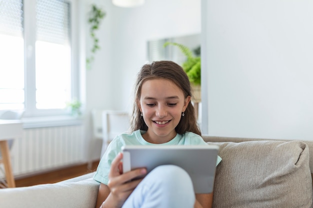 Ładny mały szczęśliwy dziewczyna uśmiech siadając na kanapie za pomocą patrząc cyfrowy tablet pad w salonie w domu. koncepcja działalności rodzinnej.