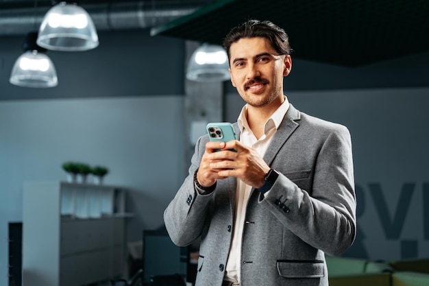 Ładny młody Arab w formalnym ubraniu używający smartfona w biurze