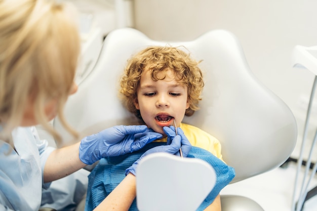 Ładny młody chłopak odwiedza dentystę, po sprawdzeniu zębów przez kobietę dentystę w gabinecie stomatologicznym.