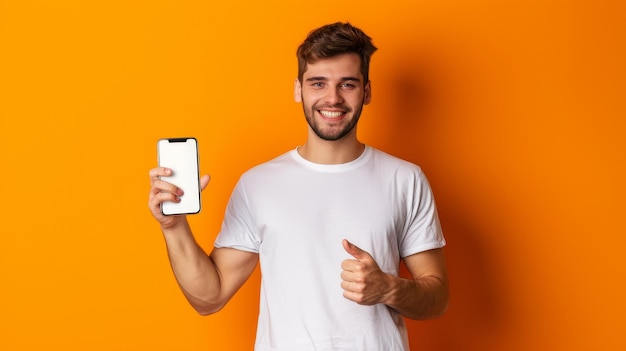 Ładny podekscytowany mężczyzna wskazuje na pusty biały ekran smartfona na pomarańczowym tle studia uśmiechając się do kamery Sprawdź model ekranu telefonu komórkowego
