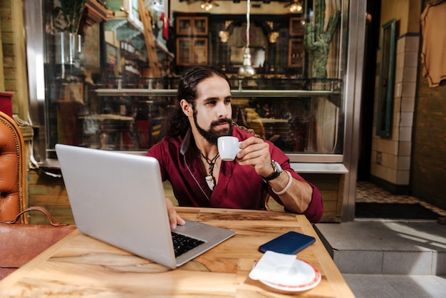 Ładny, przystojny mężczyzna, trzymając kubek z espresso podczas pracy na laptopie