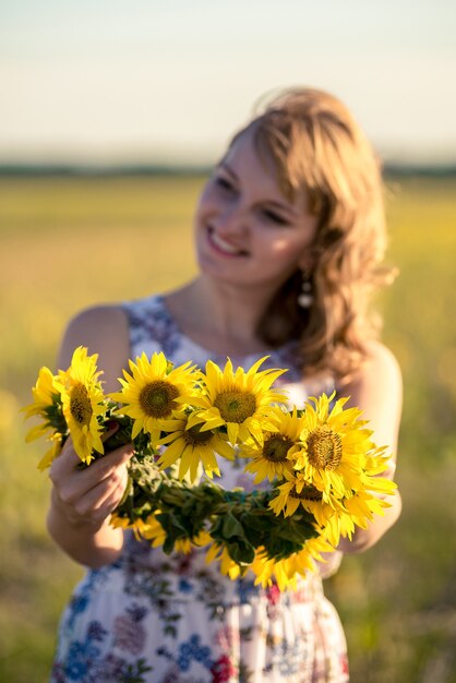Ładny redhaired niewyraźne uśmiechnięta dziewczyna w polu pełnym słoneczników, wieniec słoneczników.