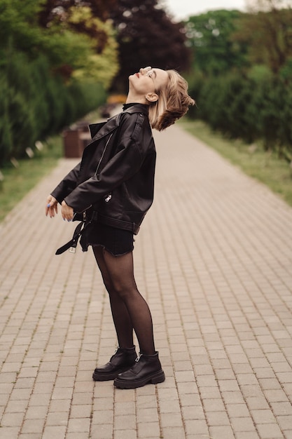 Ładny szczęśliwy dziewczyna w okularach w czarnej kurtce i sukience spacery po parku samotnie jesienią.