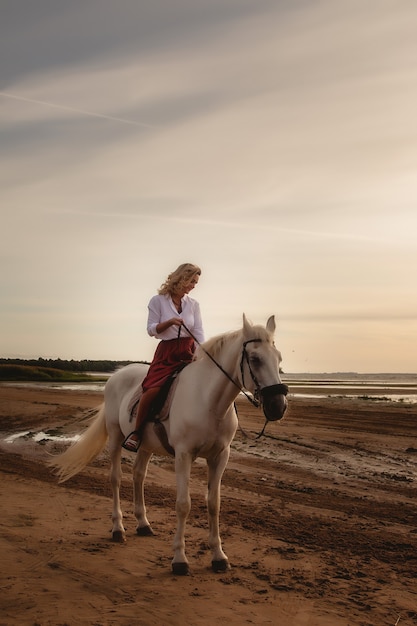 Ładny szczęśliwy młoda kobieta na koniu w lato plaża nad morzem. Kobieta jeździec jeździ swoim koniem w przyrodzie na tle zachodu słońca wieczorem światło. Koncepcja jazdy na świeżym powietrzu, sportu i rekreacji. Skopiuj miejsce