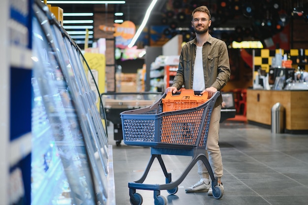 Ładny, uśmiechnięty mężczyzna robi zakupy w supermarkecie, popychając wózek.